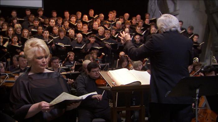 Conductor Murry Sidlin with a full chorus and orchestra at Terezin for a memorial performance of the Requiem in 2006. Below (from left): a reenactment of Rafael Schaechter at the piano; Boston-based Holocaust survivor Edgar Krasa and his sons, Raphael and Donny.